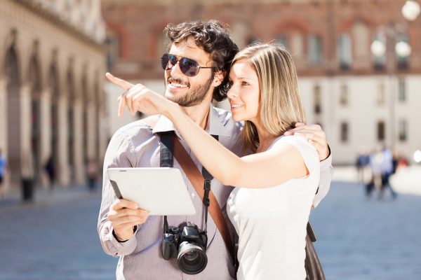 Un uomo e una donna che fanno i turisti in una piazza e osservano i luoghi orientandosi con un tablet.